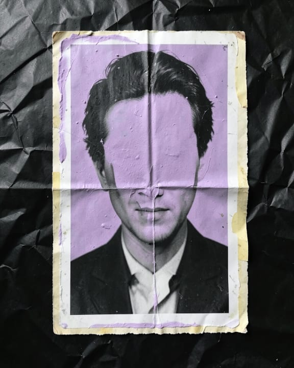 A portrait of a man in a suit with a purple band covering his eyes.
