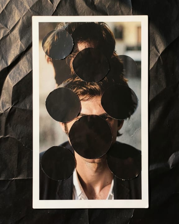 A portrait of a man is obscured by several black circular cutouts.